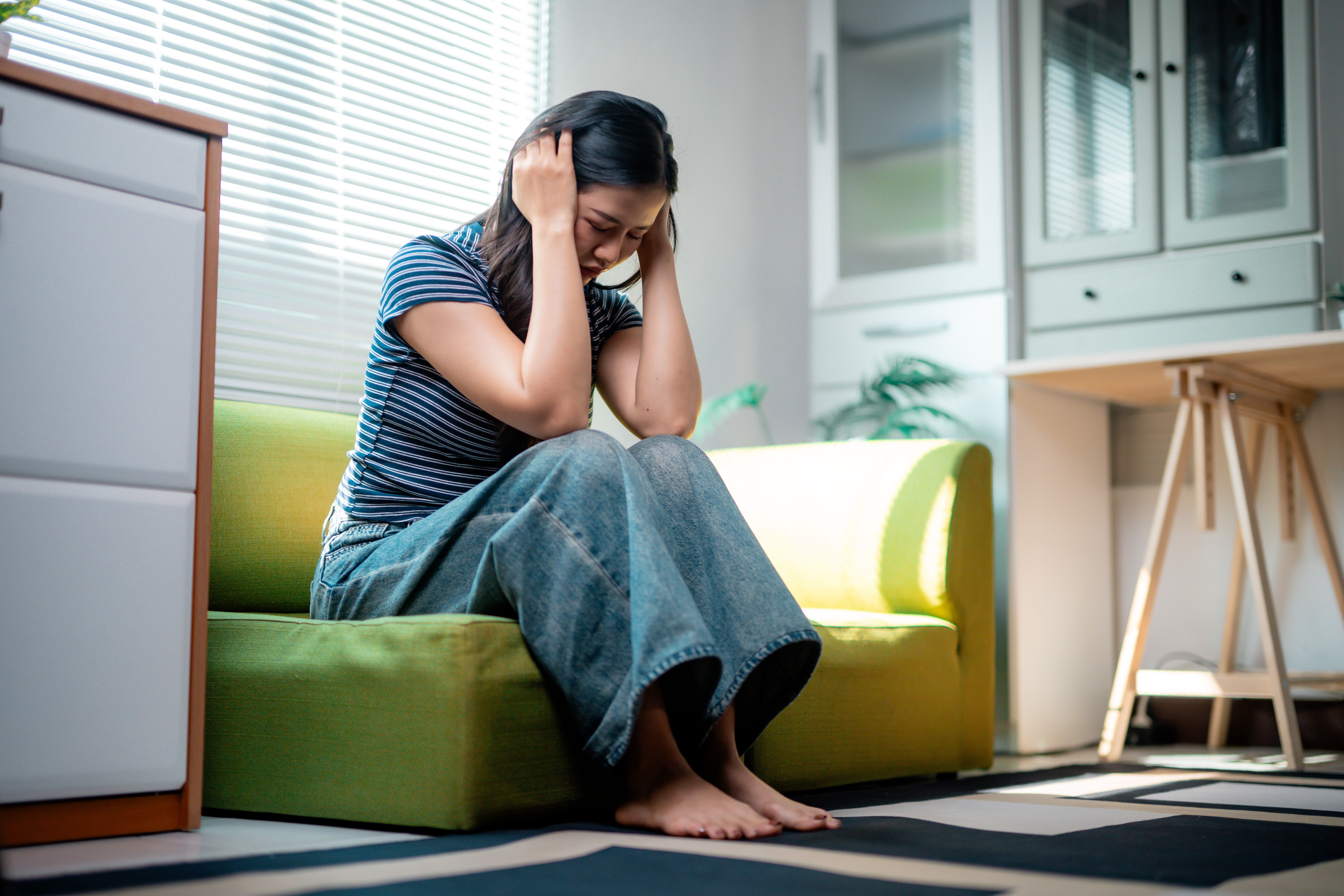 Jovem mulher asiática sentindo-se triste e deprimida em casa. A cena representa visualmente os impactos da depressão no cotidiano.
