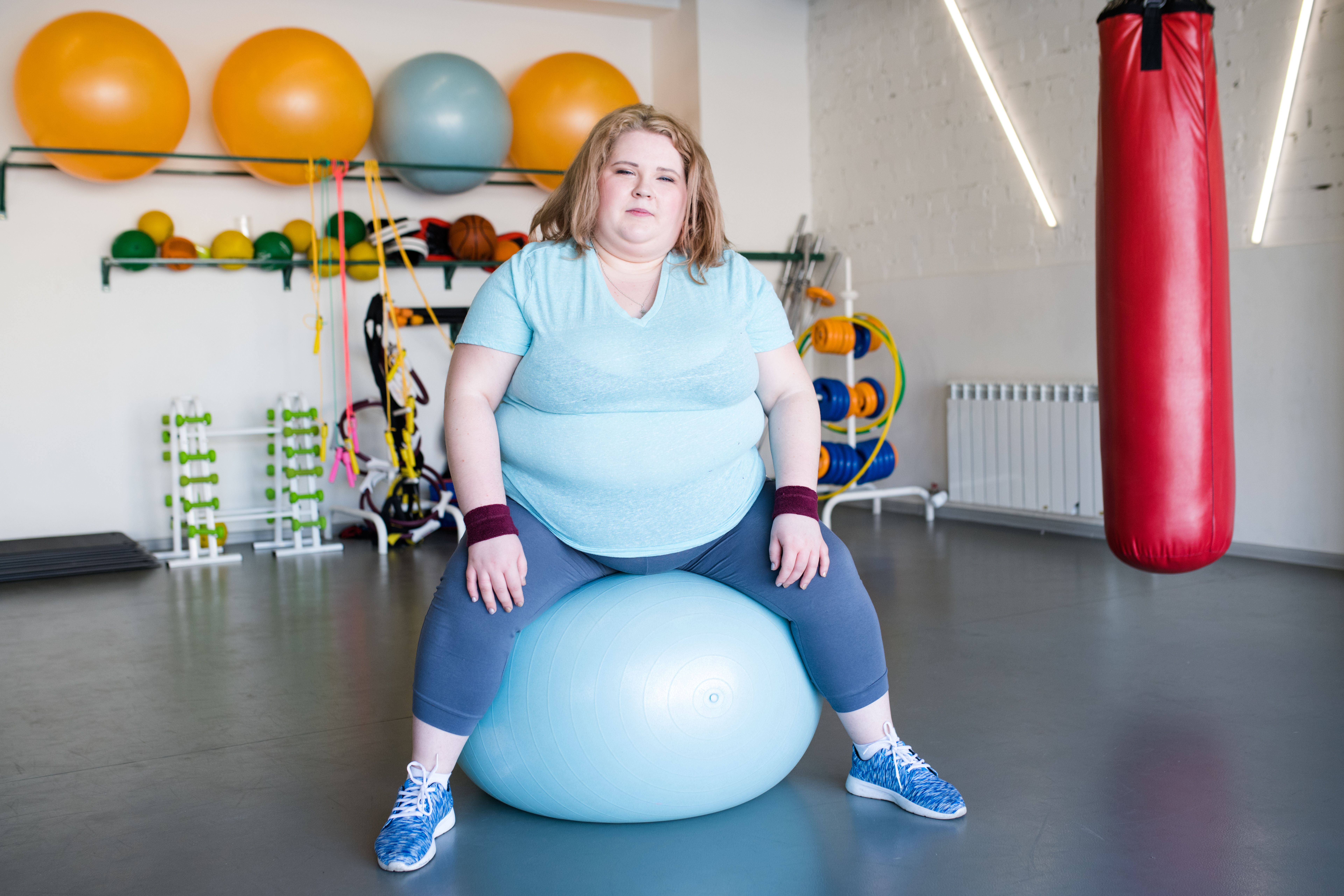 Mulher plus size sentada em bola de pilates durante treino em academia.