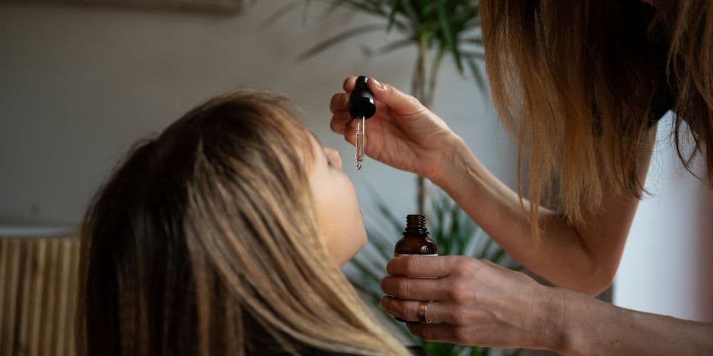 Mulher aplicando óleo de canabidiol (CBD) sob a língua de uma criança com o uso de um conta-gotas.