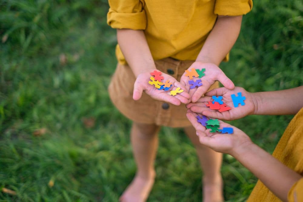 Duas crianças vestindo roupas amarelas seguram peças coloridas de um quebra-cabeça, representando o dia do autismo.
