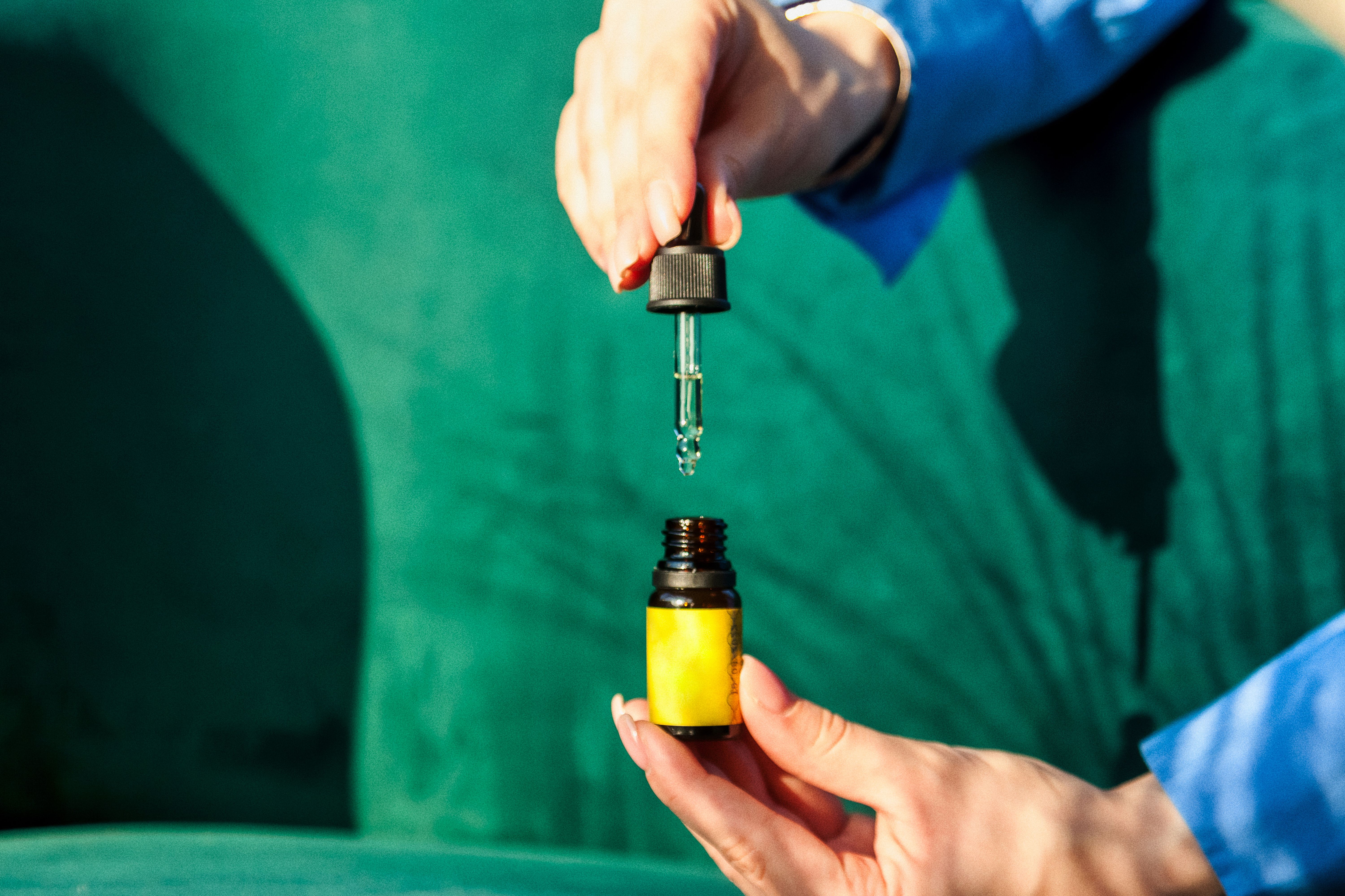 Mulher segurando um frasco pequeno de vidro âmbar com rótulo amarelo, usando um conta-gotas para retirar o líquido.