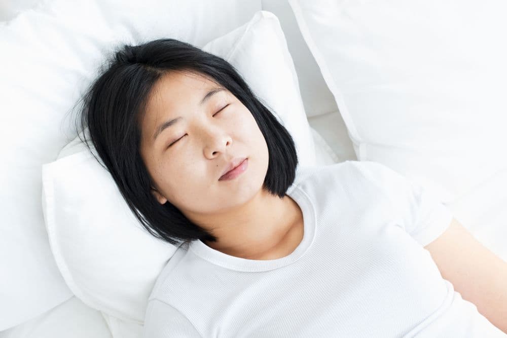 Mulher jovem dormindo em paz sobre travesseiro branco, simbolizando melhora do sono com CBD no tratamento da apneia.