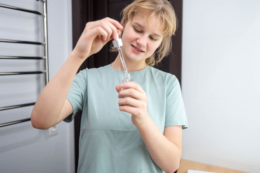 Adolescente segura frasco com conta-gotas de óleo de cannabis medicinal.