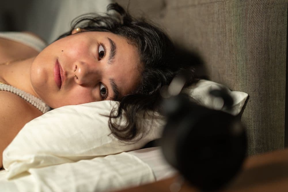 Mulher deitada na cama com insônia olhando para o despertador.