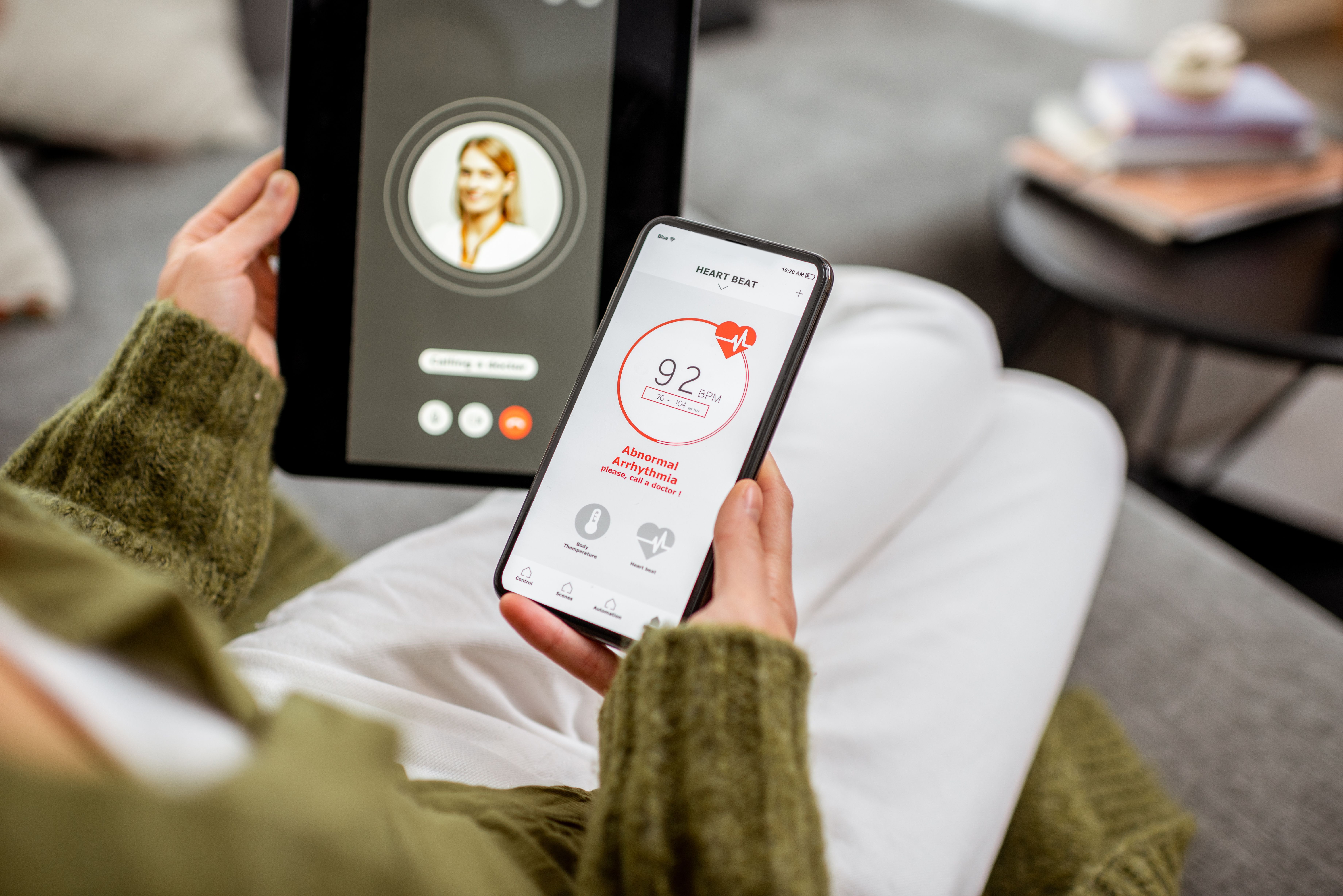 Mulher segurando smartphone com app de monitoramento cardíaco e participando de consulta médica por vídeo chamada.