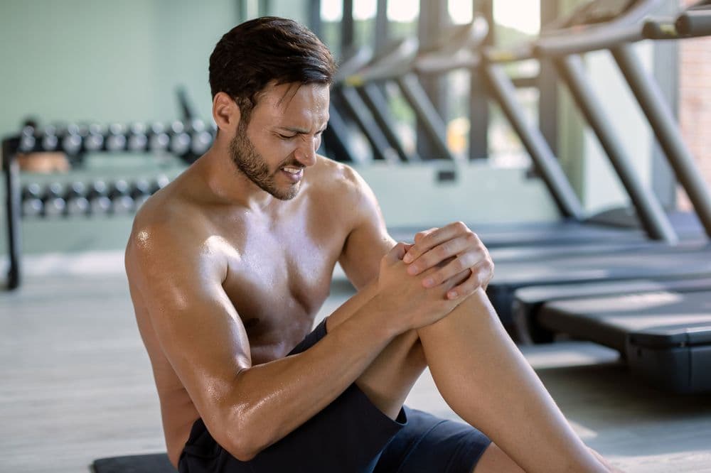 Atleta segurando o joelho com dor após treino intenso na academia, ilustrando recuperação muscular e alívio com CBD.