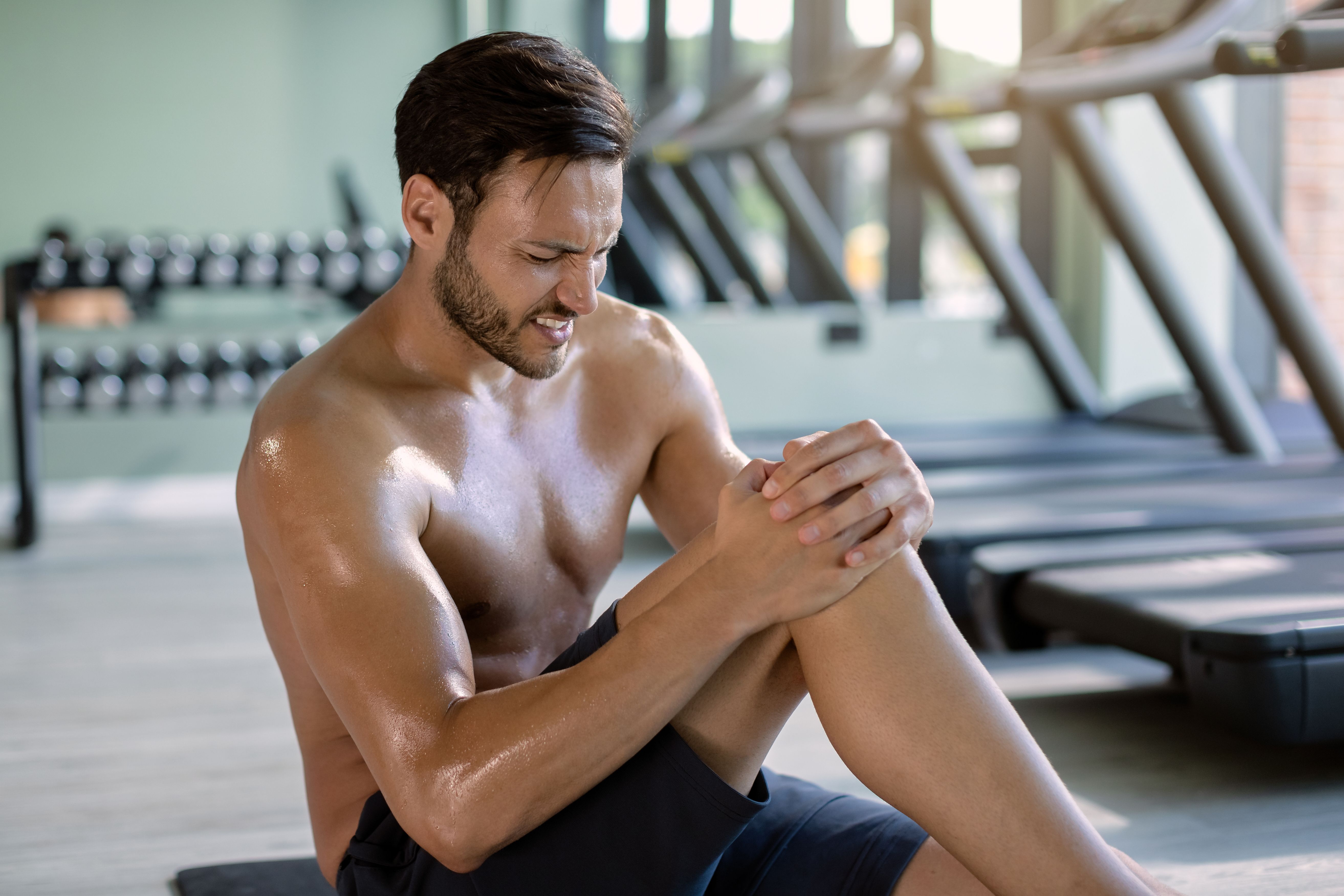 Atleta segurando o joelho com dor após treino intenso na academia, ilustrando recuperação muscular e alívio com CBD.