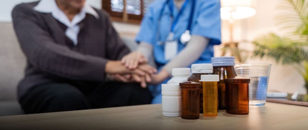 Cuidador de saúde oferecendo apoio a paciente com dor crônica, com frascos de medicamentos em destaque representando tratamento multimodal.
