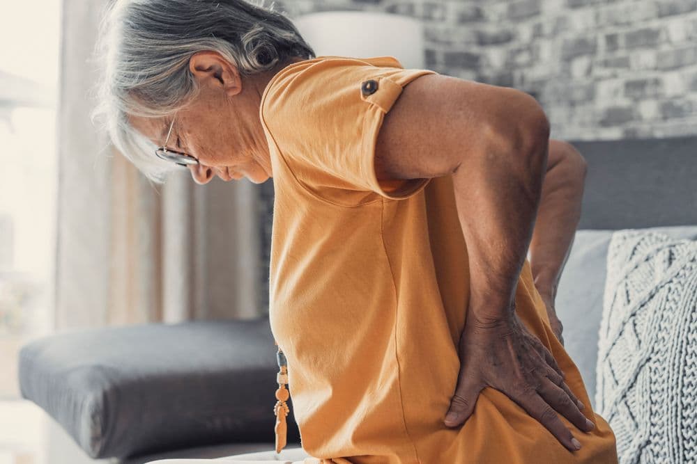 Mulher idosa com dor nas costas, representando um quadro de dor crônica e lombalgia.