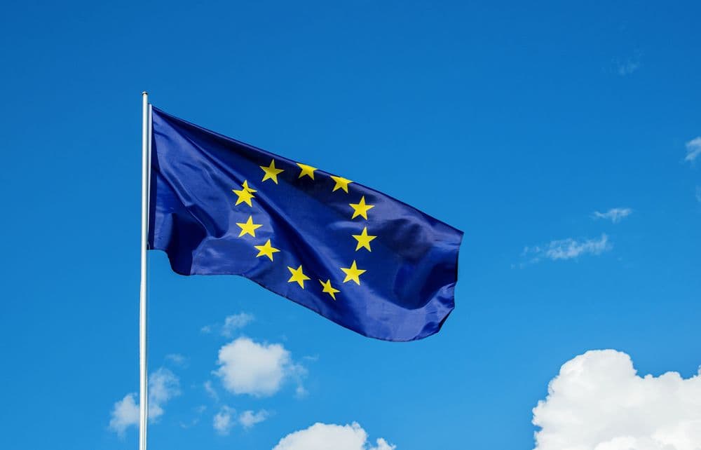  Bandeira da União Europeia tremulando contra um céu azul com algumas nuvens.