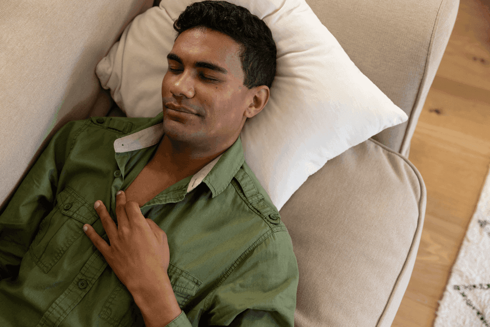 Homem de camisa verde dormindo em um sofá com expressão serena, representando os benefícios do CBD para o sono e relaxamento.