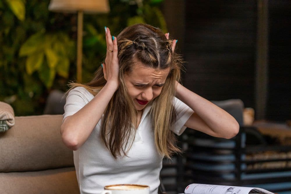 Mulher jovem segurando a cabeça com as mãos, demonstrando ansiedade e estresse durante um ataque de pânico em um ambiente interno.