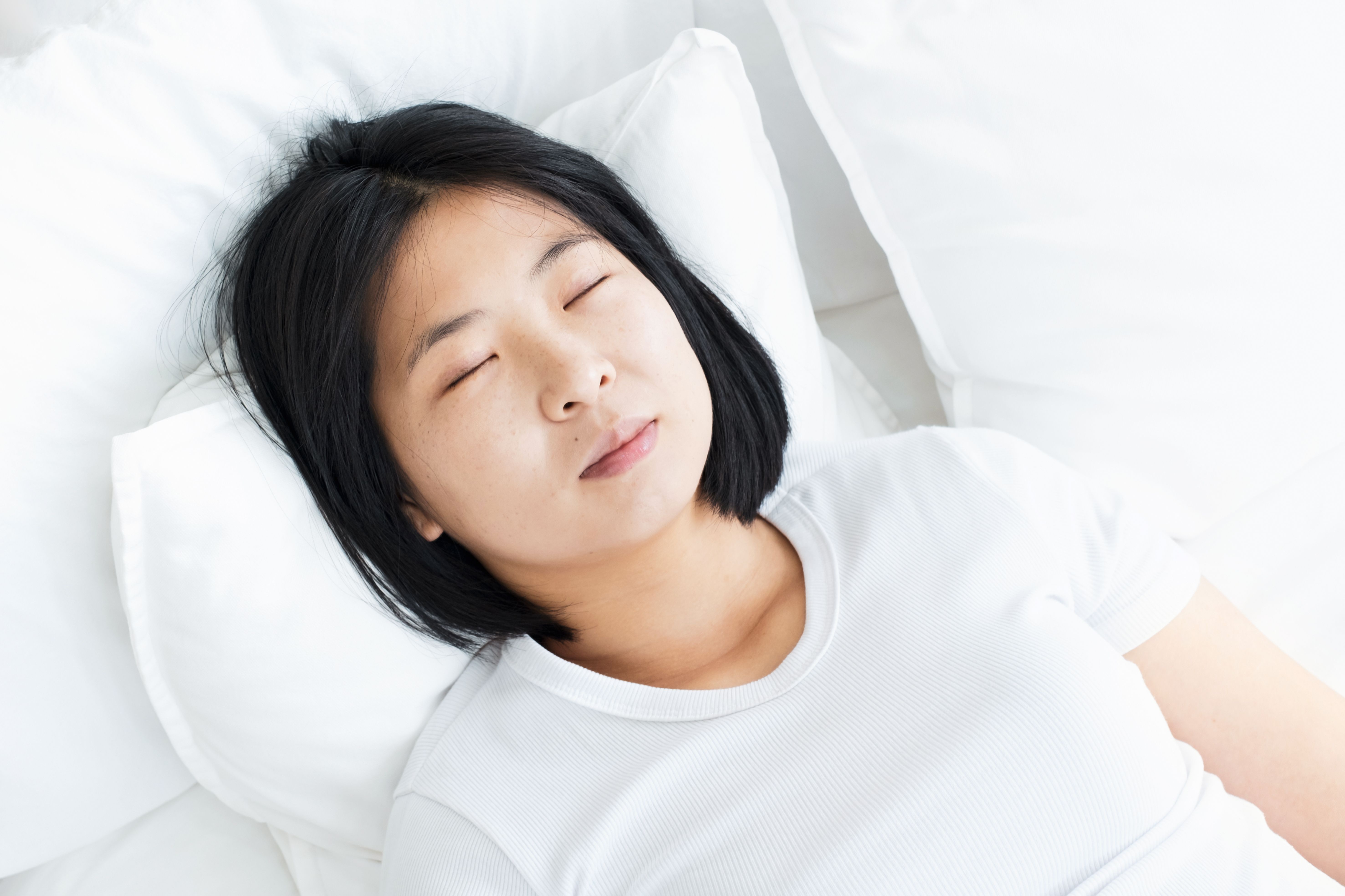 Mulher jovem dormindo em paz sobre travesseiro branco, simbolizando melhora do sono com CBD no tratamento da apneia.