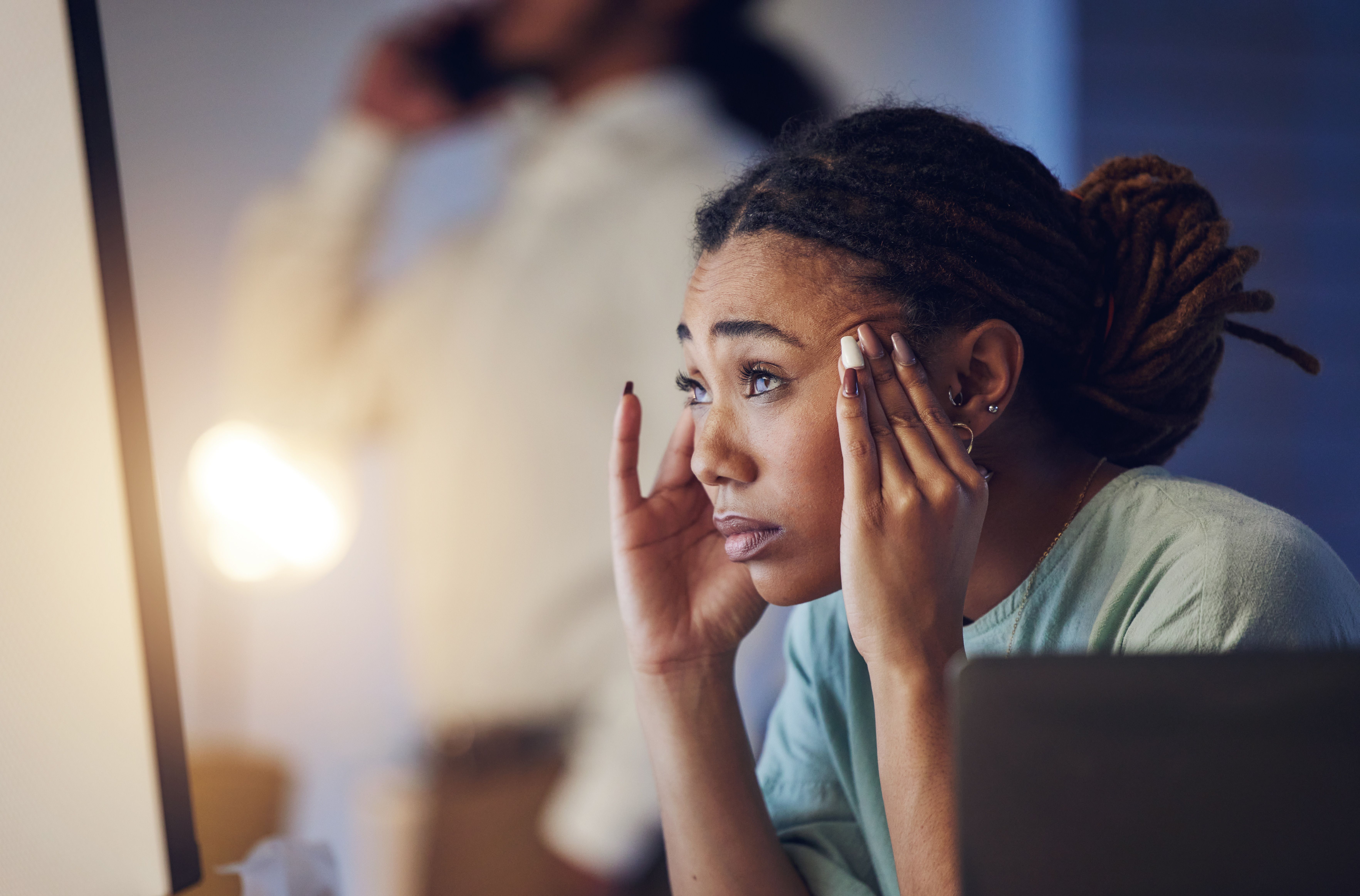 Mulher com expressão de cansaço e mãos na cabeça em frente ao computador, representando estresse e ansiedade.