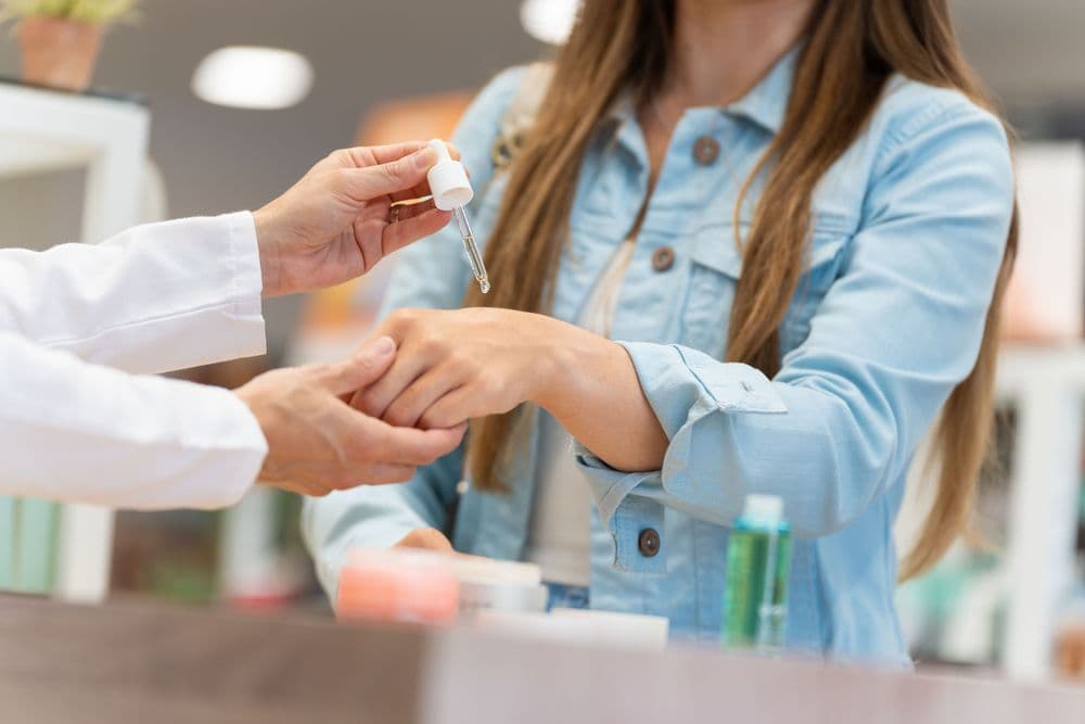 Profissional aplicando óleo tópico na mão de uma mulher, ilustrando o uso de produtos à base de cannabis para cuidados com a pele.