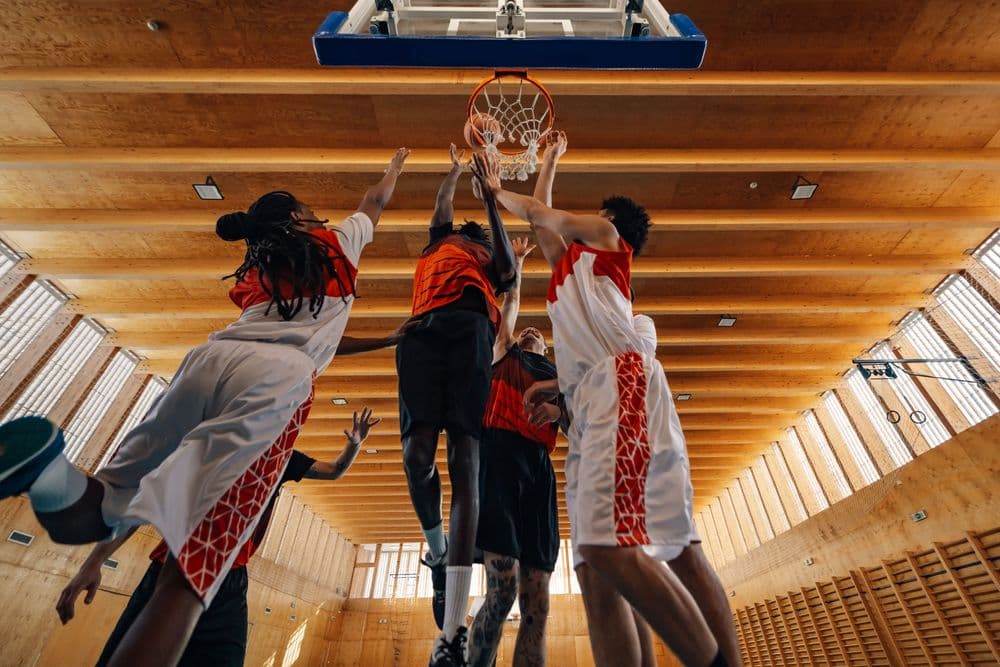 Jogadores de basquete disputando bola perto da cesta em partida indoor