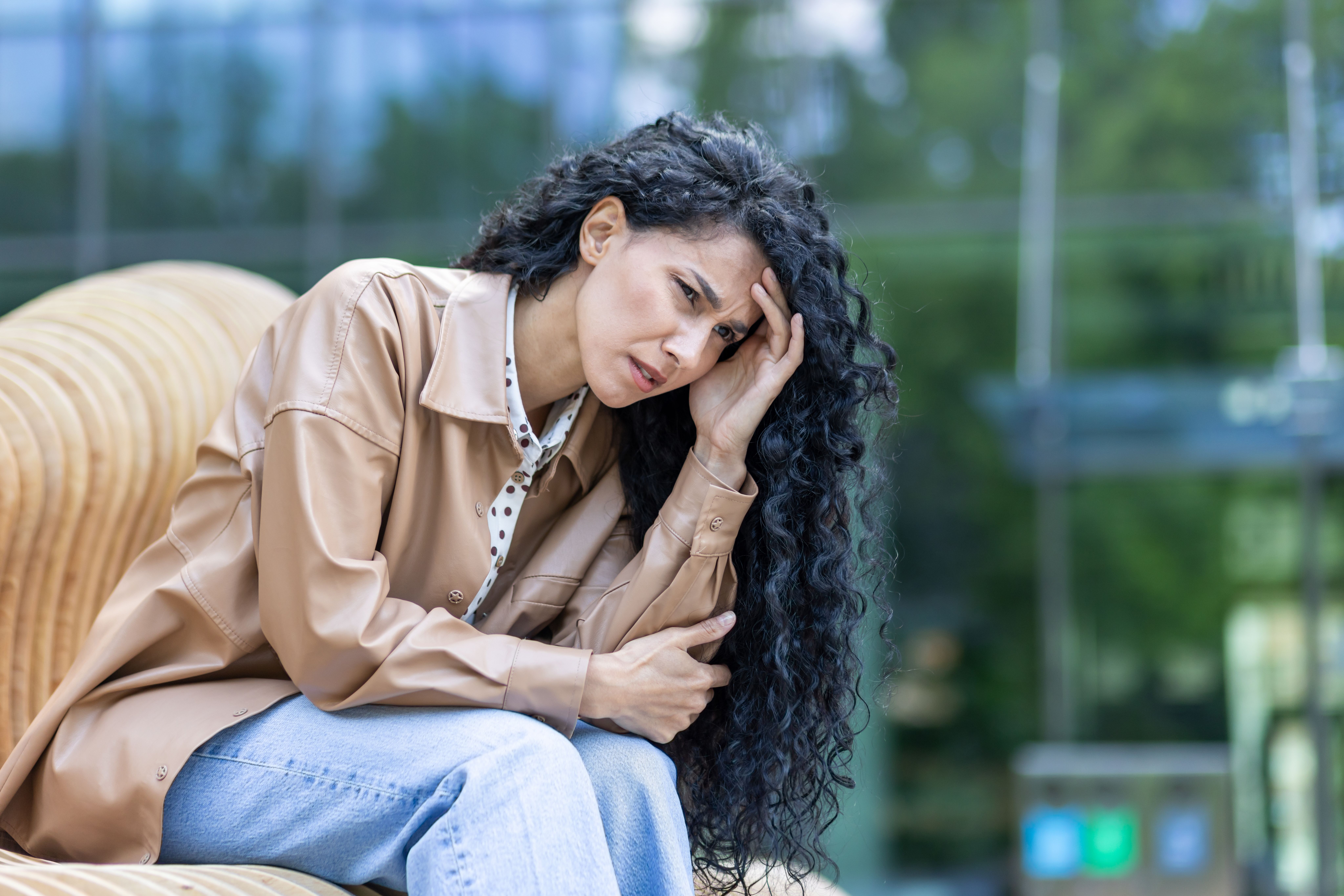 Mulher com expressão triste e preocupada, sentada sozinha, representando sinais de depressão.